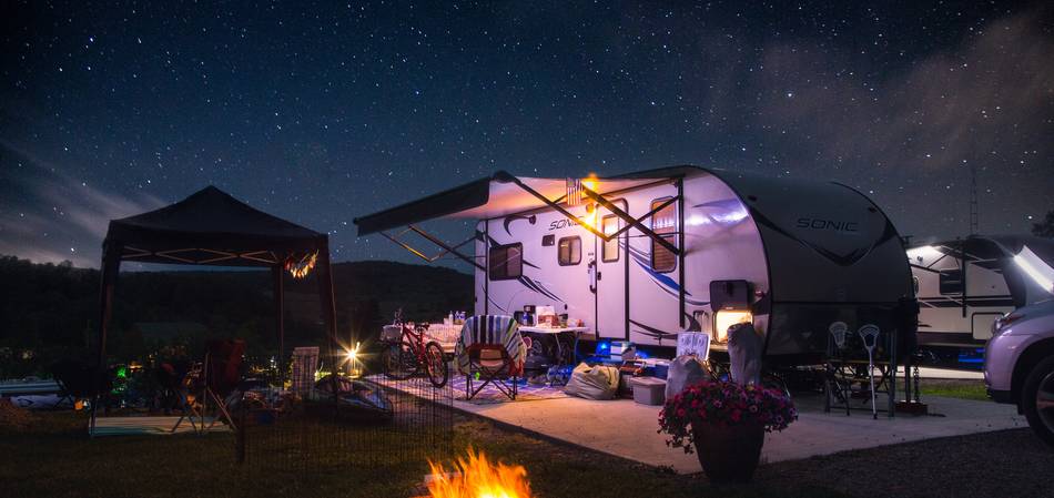 Wohnwagen bei Nacht mit Sternenhimmel und Feuer