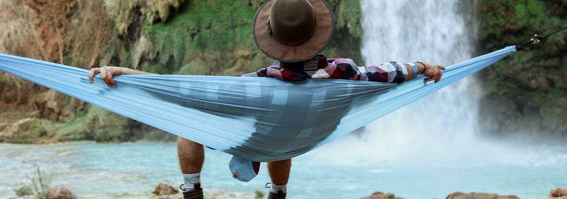 Mann mit Hut in Hängematte vor Wasserfall